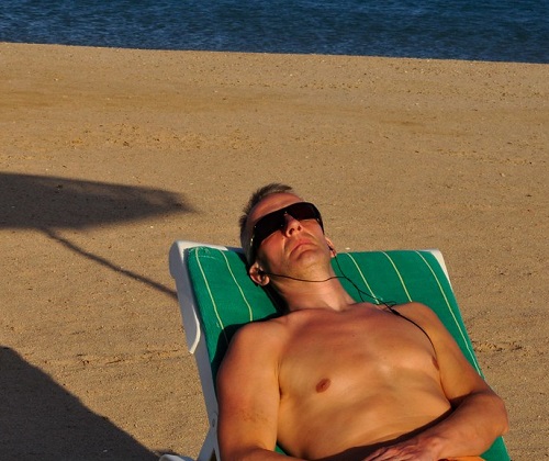 a man laying on the beach wearing sunglasses
